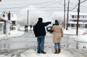 Two people watch the waves crash in the distance during a winter nor'easter snow storm in Scituate