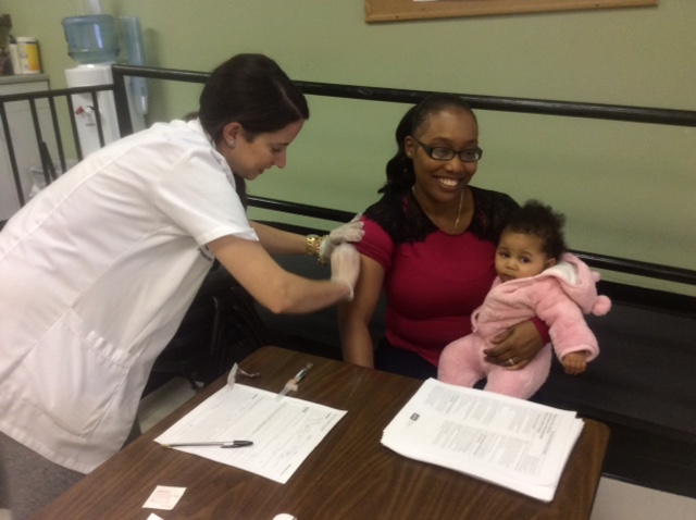 Ms. Tameka Santiago with her eight month old daughter receiving flu vaccination from Maria Troia, PharmD Pharmacy Manager, Walgreens