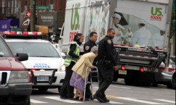 A crossing guard and two police officers assist an elderly woman crossing the street in Morris Park. Photo by David Greene