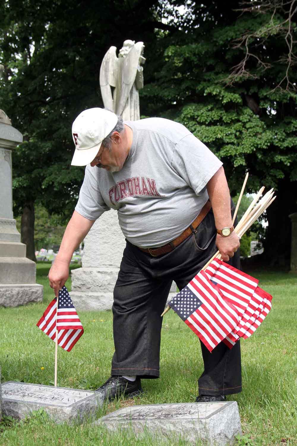 Longtime Norwood resident Bruce Campbell places a flag at the grave of military veteran Arnold Stillman.--Photo by David Greene