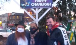 Rabbi Pewzner, Yosef Abrerra, and Gene DeFrancis stand in front of the lit menorah.